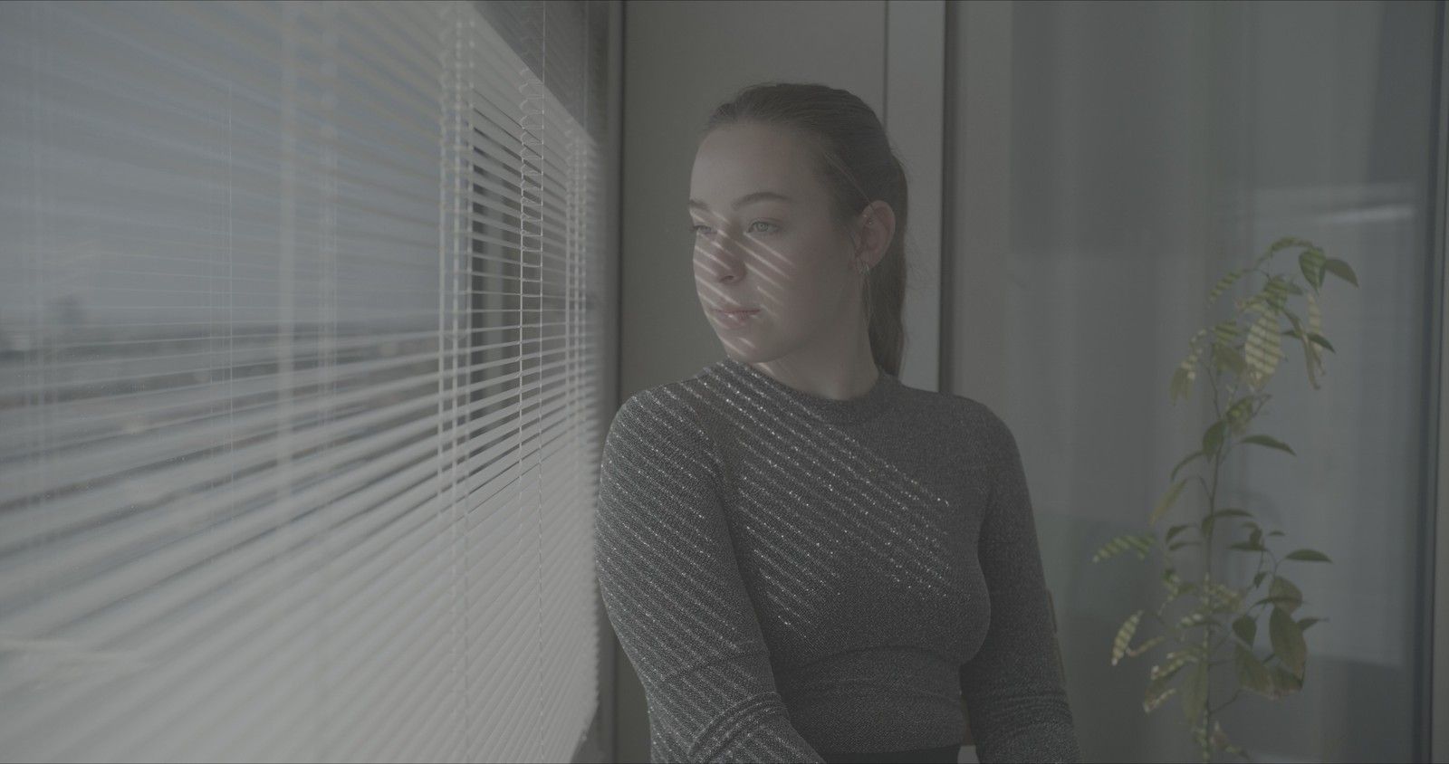 Flat log footage of a woman by window blinds
